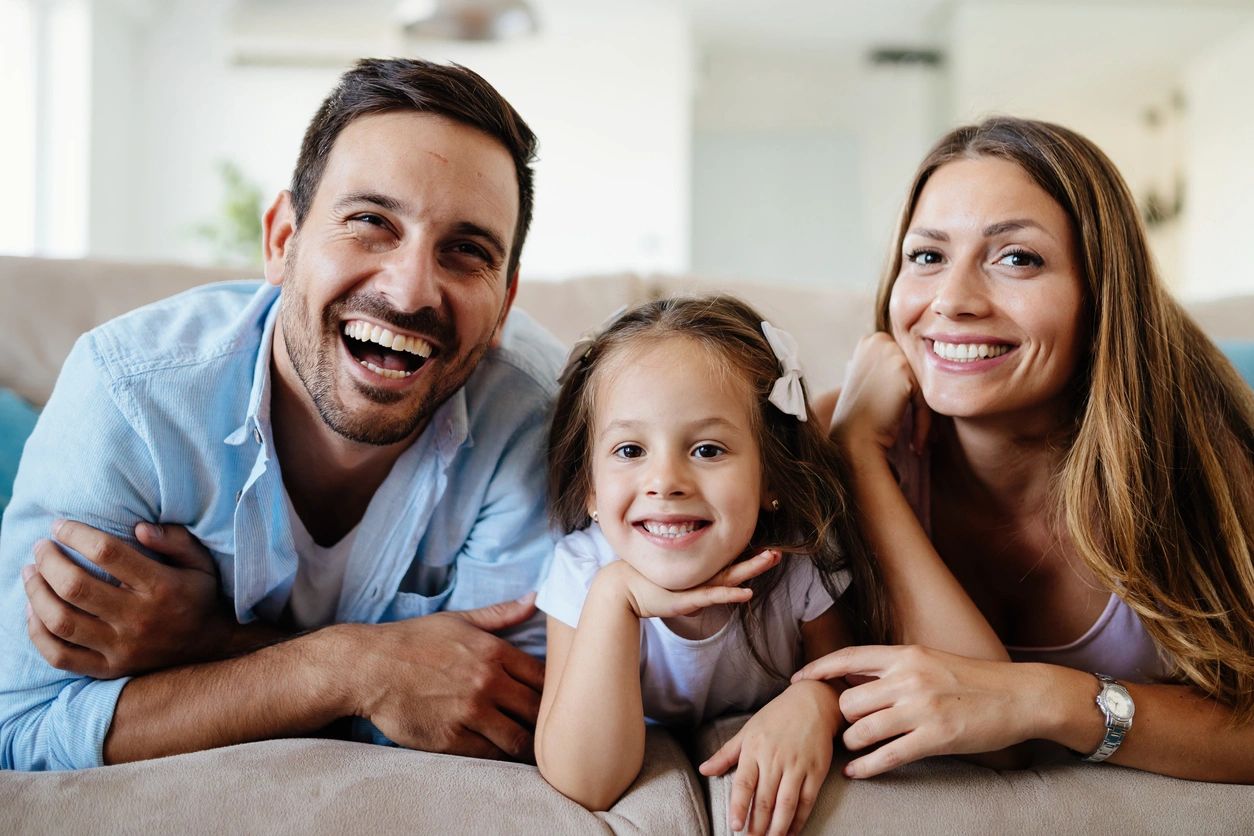 A family is laying on the couch smiling.